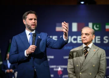 Due delegati discutono durante un vertice con bandiere nazionali sullo sfondo.