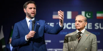 Due delegati discutono durante un vertice con bandiere nazionali sullo sfondo.