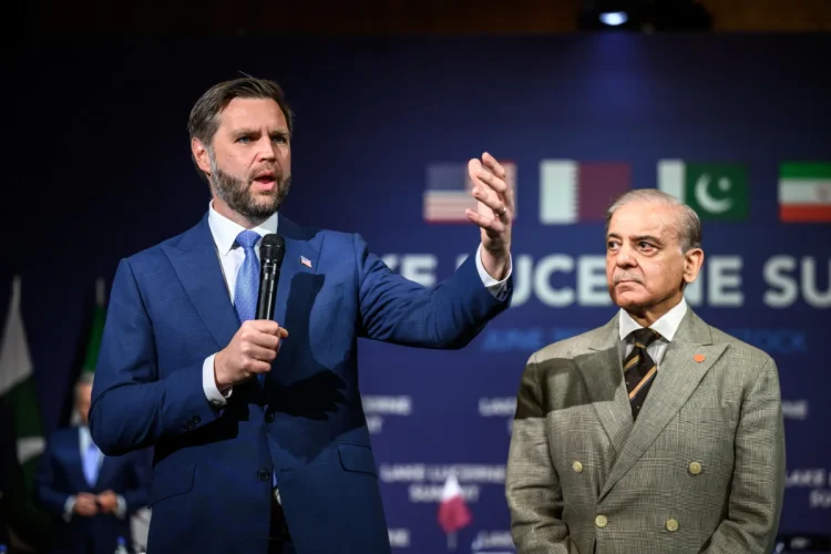 Due delegati discutono durante un vertice con bandiere nazionali sullo sfondo.