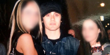 Jared Leto indossa cappello e giacca jeans tra due figure femminili sfocate. Jared Leto accusato da quattro donne di violenza sessuale