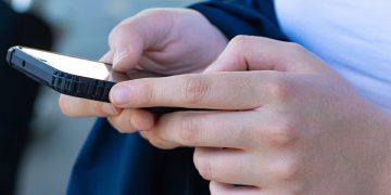 Ragazzo con in mano un telefono. Recensioni online l'Antitrust chiede lo scontrino per verificarne l'autenticità