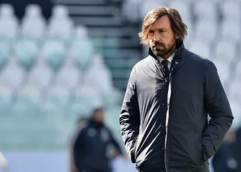 Andrea Pirlo pensieroso in campo, giacca scura, sfondo stadio.
