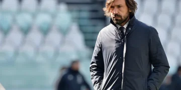 Andrea Pirlo pensieroso in campo, giacca scura, sfondo stadio.