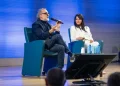 Massimo Bottura parla al microfono con donna sorridente accanto.