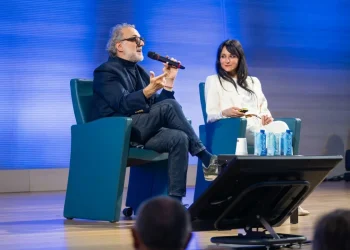 Massimo Bottura parla al microfono con donna sorridente accanto.