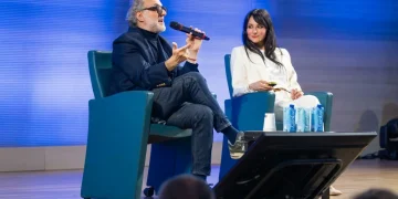 Massimo Bottura parla al microfono con donna sorridente accanto.