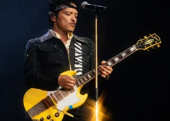 Bruno Mars suona la chitarra elettrica gialla durante un concerto dal vivo.