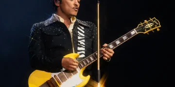 Bruno Mars suona la chitarra elettrica gialla durante un concerto dal vivo.