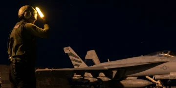 Membro personale di terra dirige F-18 Hornet su portaerei di notte.