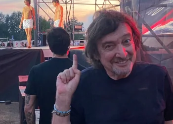 Claudio Cecchetto sorride indica, dietro giovani in boxer bianchi su palco