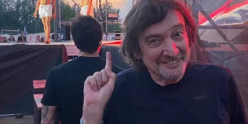 Claudio Cecchetto sorride indica, dietro giovani in boxer bianchi su palco
