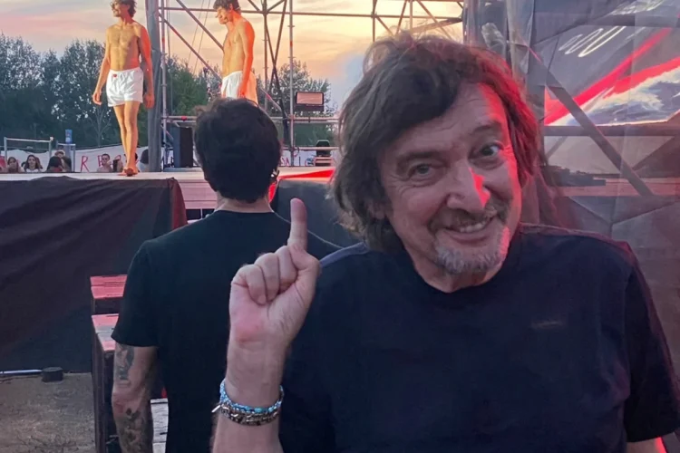 Claudio Cecchetto sorride indica, dietro giovani in boxer bianchi su palco