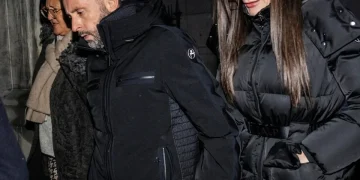 Coppia cammina di sera tenendosi per mano, sguardi seri e cappotti invernali.