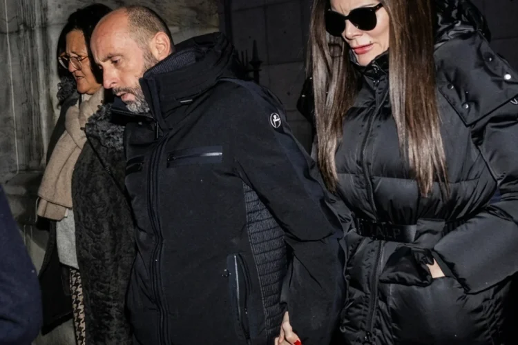 Coppia cammina di sera tenendosi per mano, sguardi seri e cappotti invernali.
