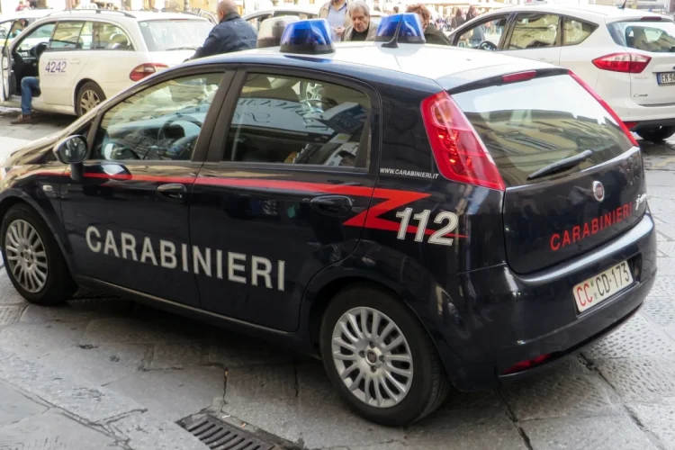 Auto dei Carabinieri parcheggiata, persone si muovono nello sfondo