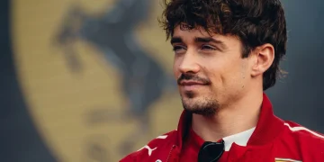 Charles Leclerc vestito Ferrari con giacca rossa, occhiali da sole appesi