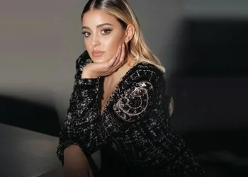 Donna bionda con giacca nera brillante in posa elegante