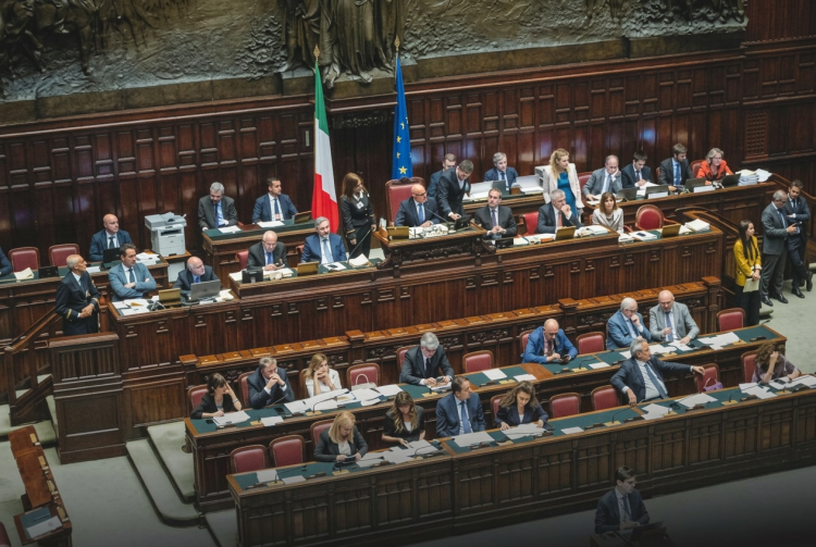 Deputati siedono nell'aula parlamentare italiana con bandiere visibili, focus sull'assemblea. Riforma elettorale, ok dalla Camera con 217 sì: il testo va al Senato tra le tensioni di governo