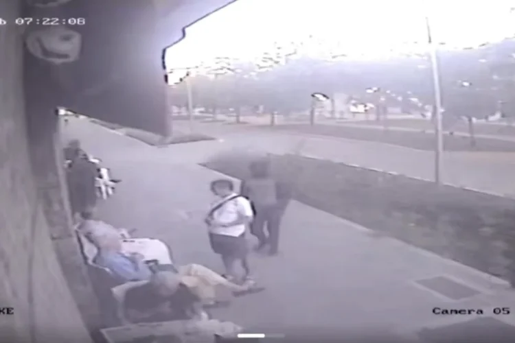 Persone sedute e in piedi su marciapiede, riprese telecamera di sorveglianza.