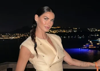 Melissa Satta sorride in abito beige su balcone notturno.