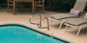 Piscina all'aperto con sdraio, tavolo in legno e vegetazione rigogliosa