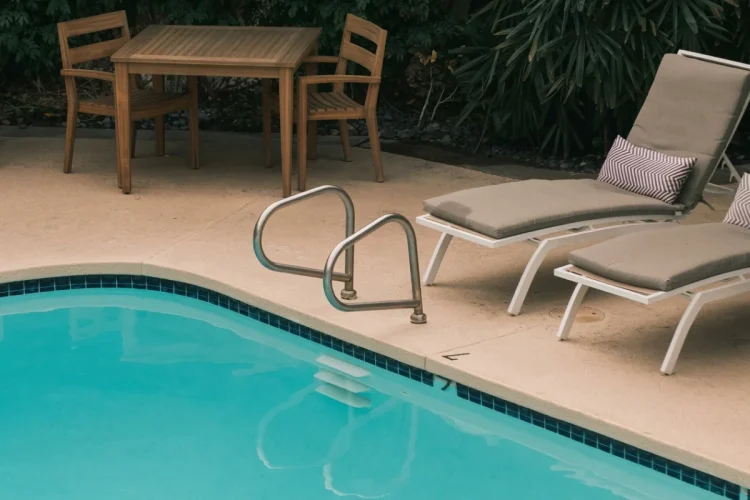 Piscina all'aperto con sdraio, tavolo in legno e vegetazione rigogliosa