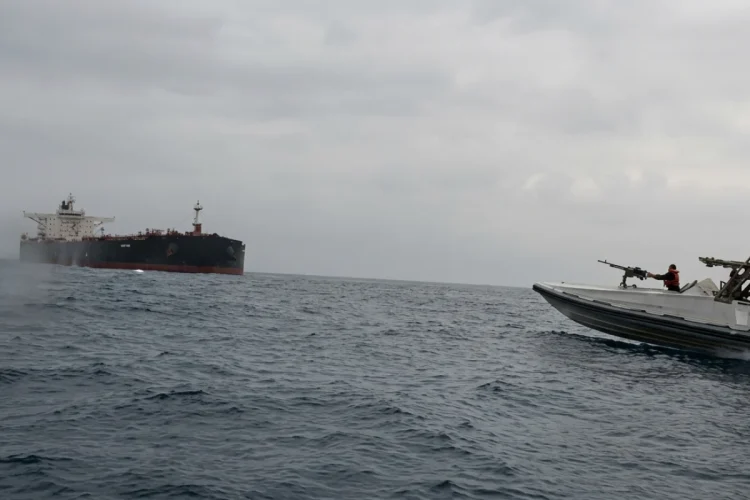 Nave militare con soldati insegue una grande petroliera in mare aperto.