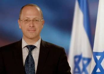 Dmitry Safronov in giacca e cravatta davanti a bandiere israeliane.