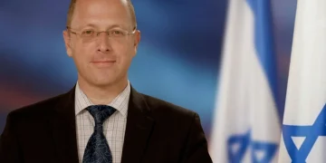 Dmitry Safronov in giacca e cravatta davanti a bandiere israeliane.