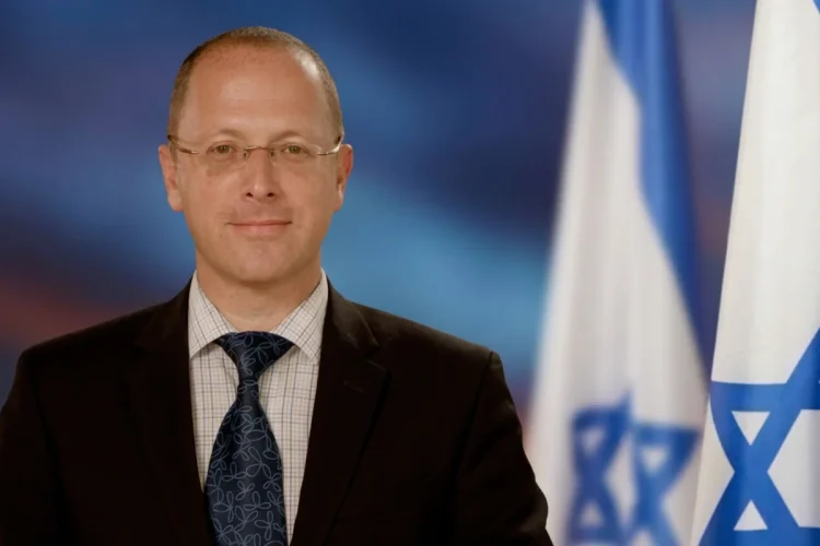 Dmitry Safronov in giacca e cravatta davanti a bandiere israeliane.