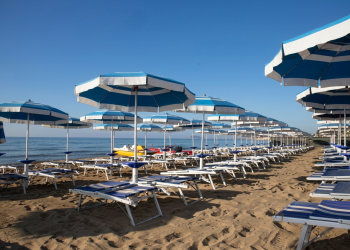 Ombrelloni e lettini allineati su una spiaggia di sabbia chiara. Ancona, tromba d'aria al Passetto: ombrelloni e lettini volano in aria