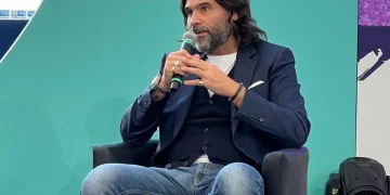Lele Adani in primo piano siede e parla al microfono