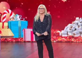 Mara Venier sorride in studio con abito scuro e occhiali.