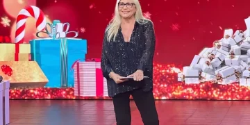 Mara Venier sorride in studio con abito scuro e occhiali.