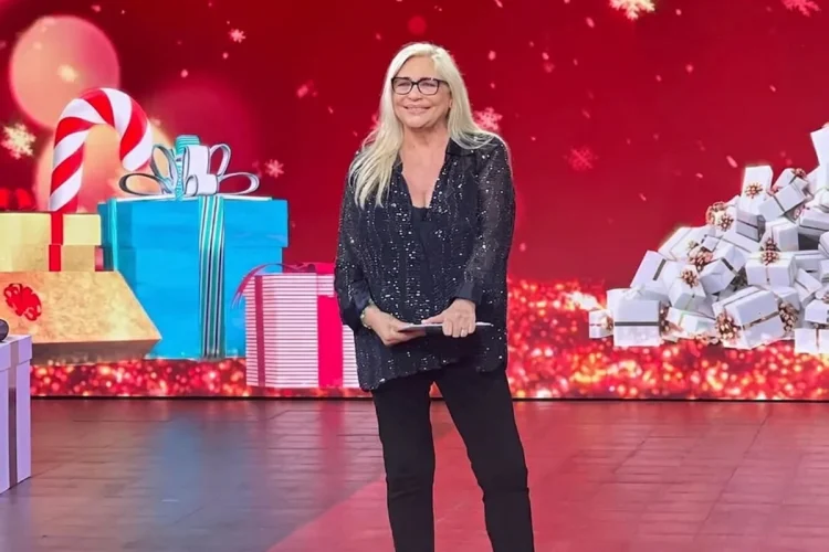 Mara Venier sorride in studio con abito scuro e occhiali.