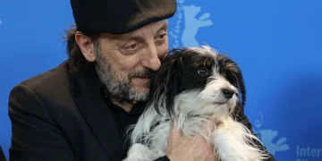 Massimo Ceccherini tiene in braccio un cane bianco e nero su sfondo blu.