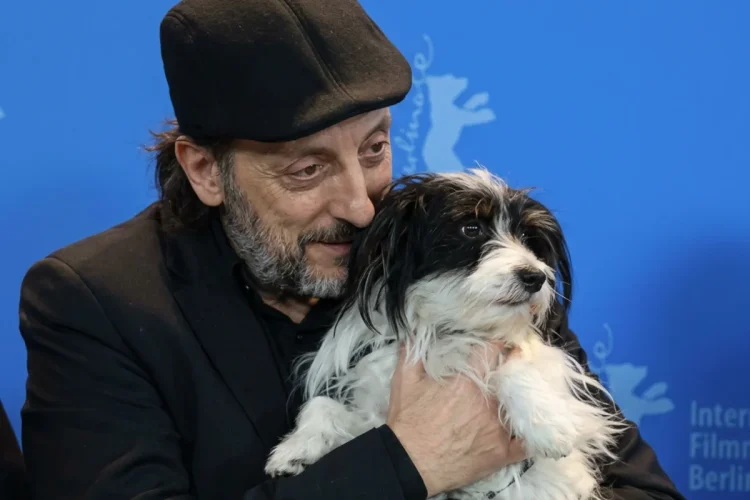 Massimo Ceccherini tiene in braccio un cane bianco e nero su sfondo blu.
