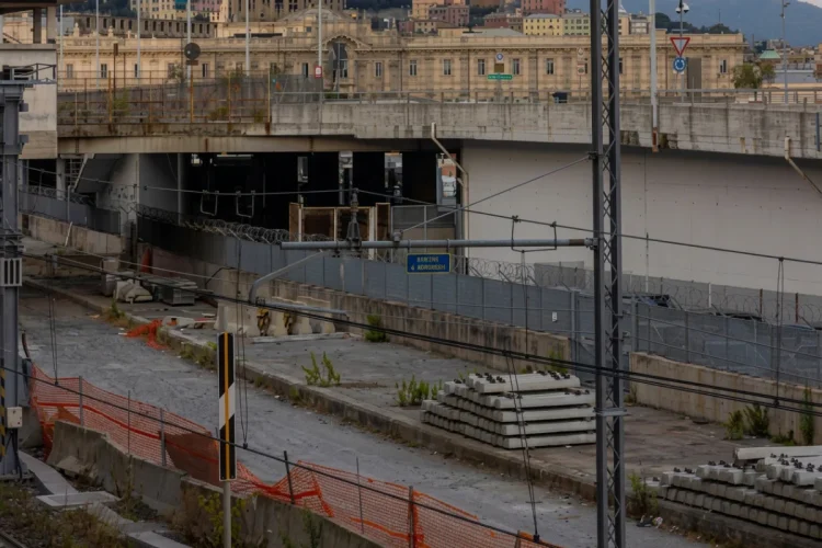 Cantiere ferroviario con traversine di cemento e barriere arancioni.