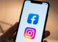 Smartphone mostra loghi Facebook e Instagram su sfondo bianco.