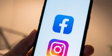 Smartphone mostra loghi Facebook e Instagram su sfondo bianco.