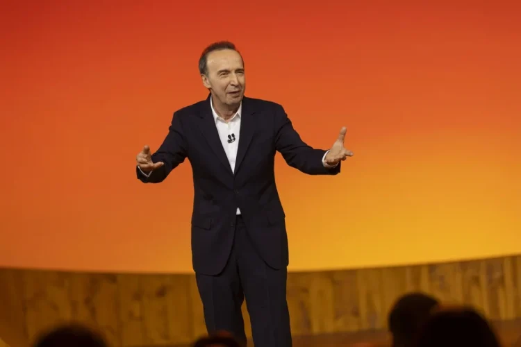 Roberto Benigni gesticola sul palco con un completo scuro