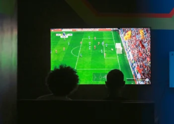 Due persone osservano una partita di calcio su schermo televisivo al buio