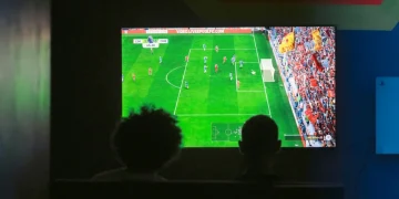 Due persone osservano una partita di calcio su schermo televisivo al buio