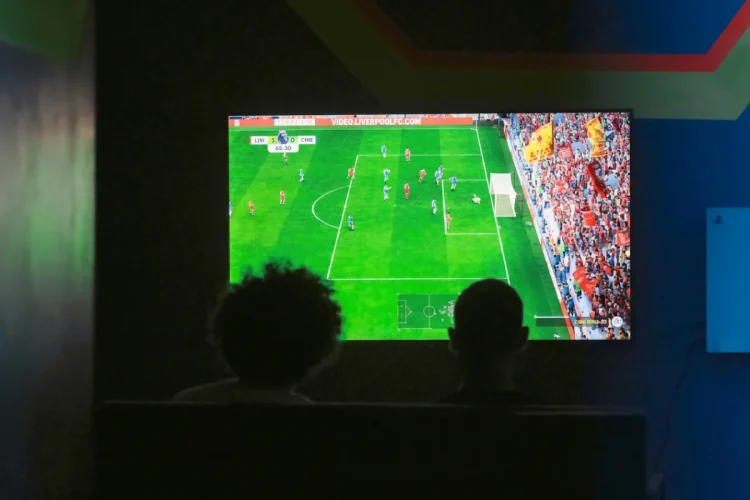 Due persone osservano una partita di calcio su schermo televisivo al buio