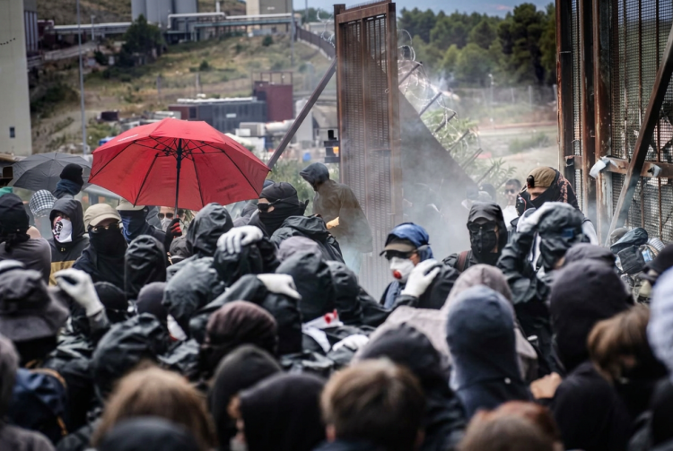 Folla di manifestanti protesta con passamontagna vicino a barriera metallica. Fermati quattro stranieri per violenze ai cantieri Tav, ipotesi devastazione al vaglio