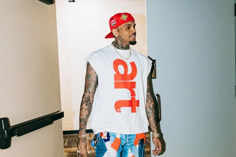 Chris Brown cammina con cappellino rosso e jeans patchwork