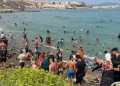 Numerosi migranti nuotano e camminano sulla spiaggia affollata di Ceuta.