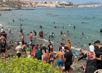 Numerosi migranti nuotano e camminano sulla spiaggia affollata di Ceuta.