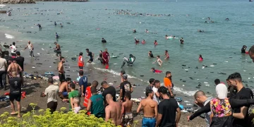 Numerosi migranti nuotano e camminano sulla spiaggia affollata di Ceuta.