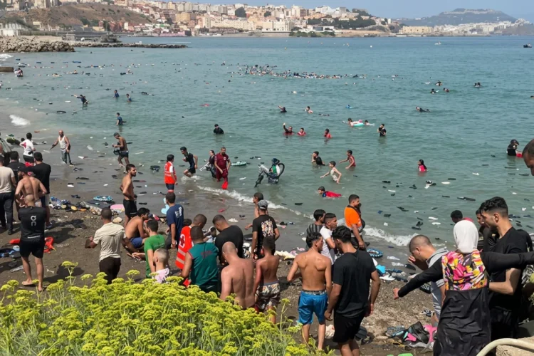 Numerosi migranti nuotano e camminano sulla spiaggia affollata di Ceuta.